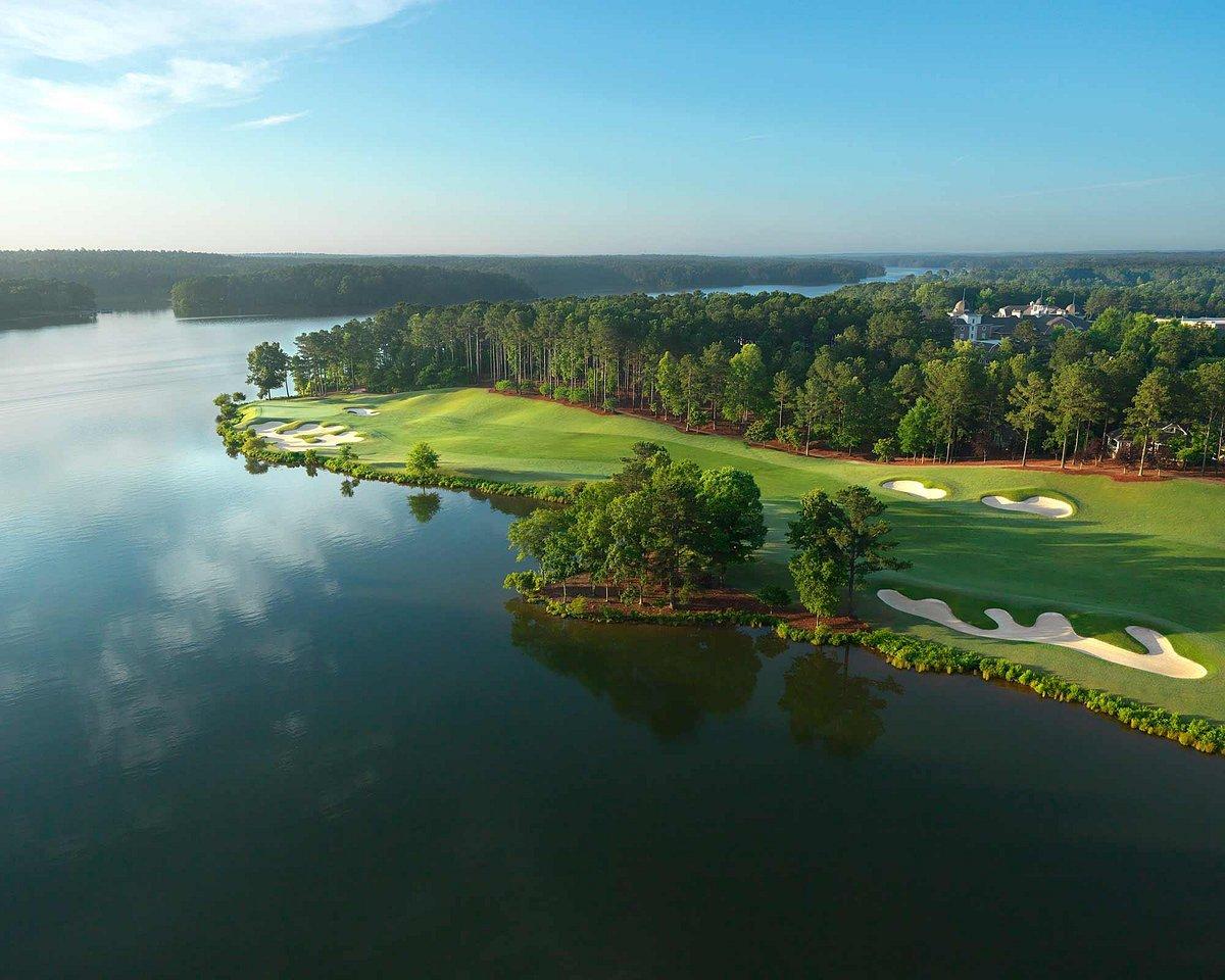 A wide fairway nestled with trees next to a large lake at The Oconee Course