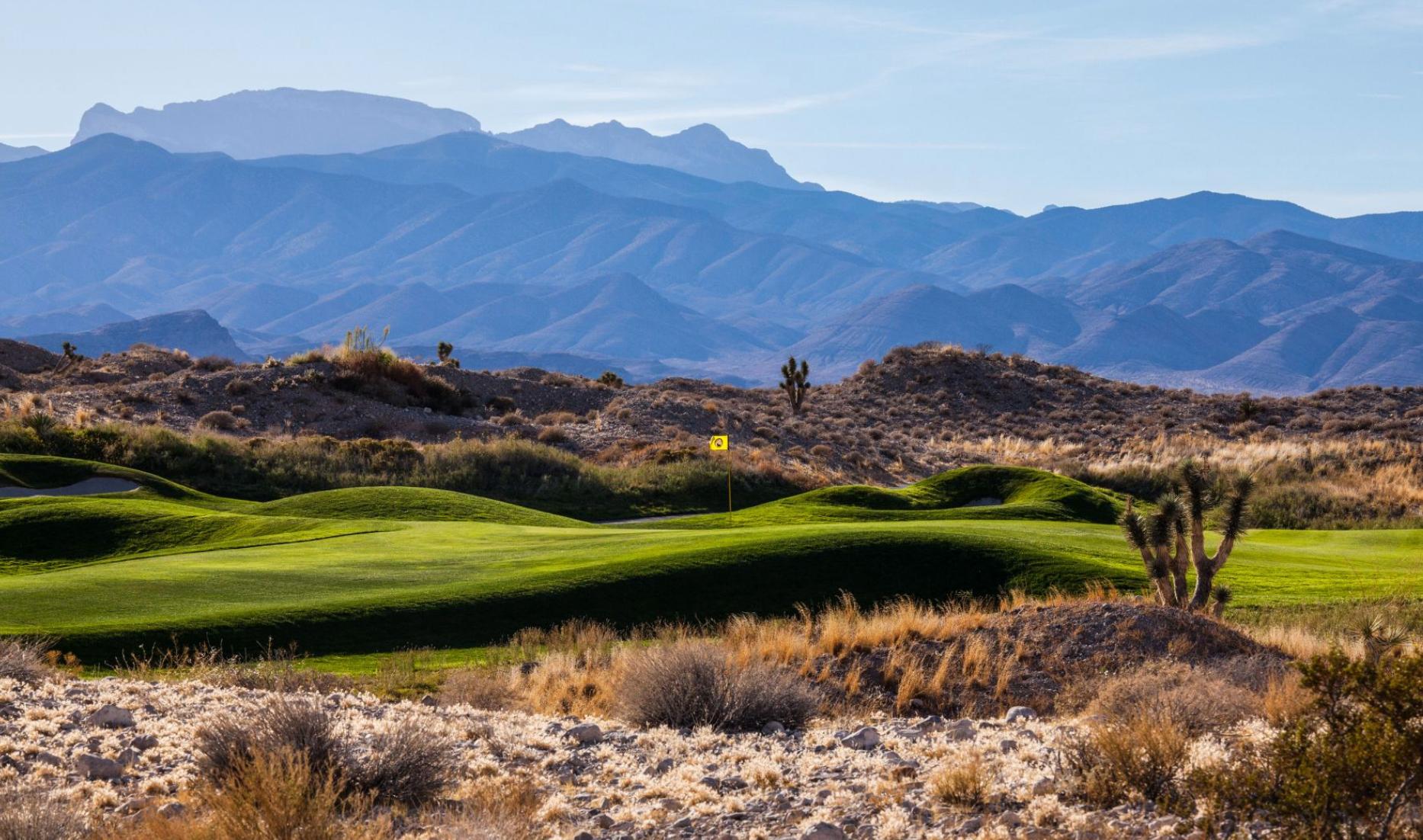 Extreme mountains towering over a smooth green surrounded by rolling dunes