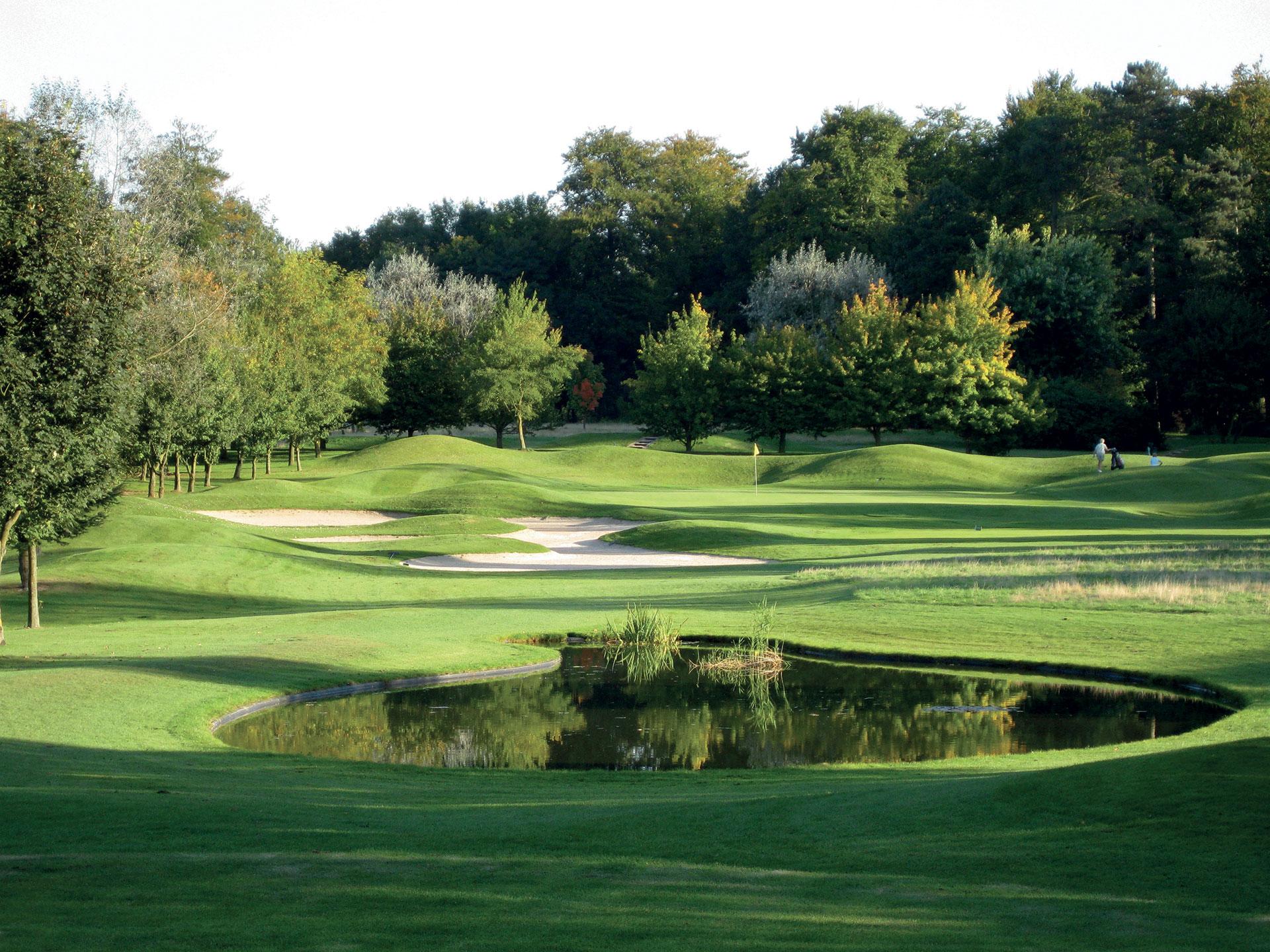 A smooth green surrounded by rolling dunes and sand bunkers under cloudy skies