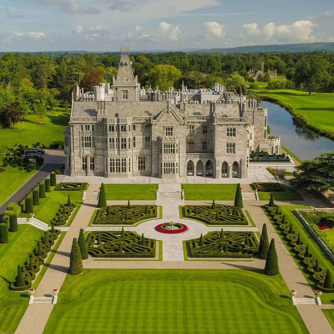 Adare Manor, a majestic castle resort, overlooks manicured gardens and a peaceful river, blending luxury with historic charm.