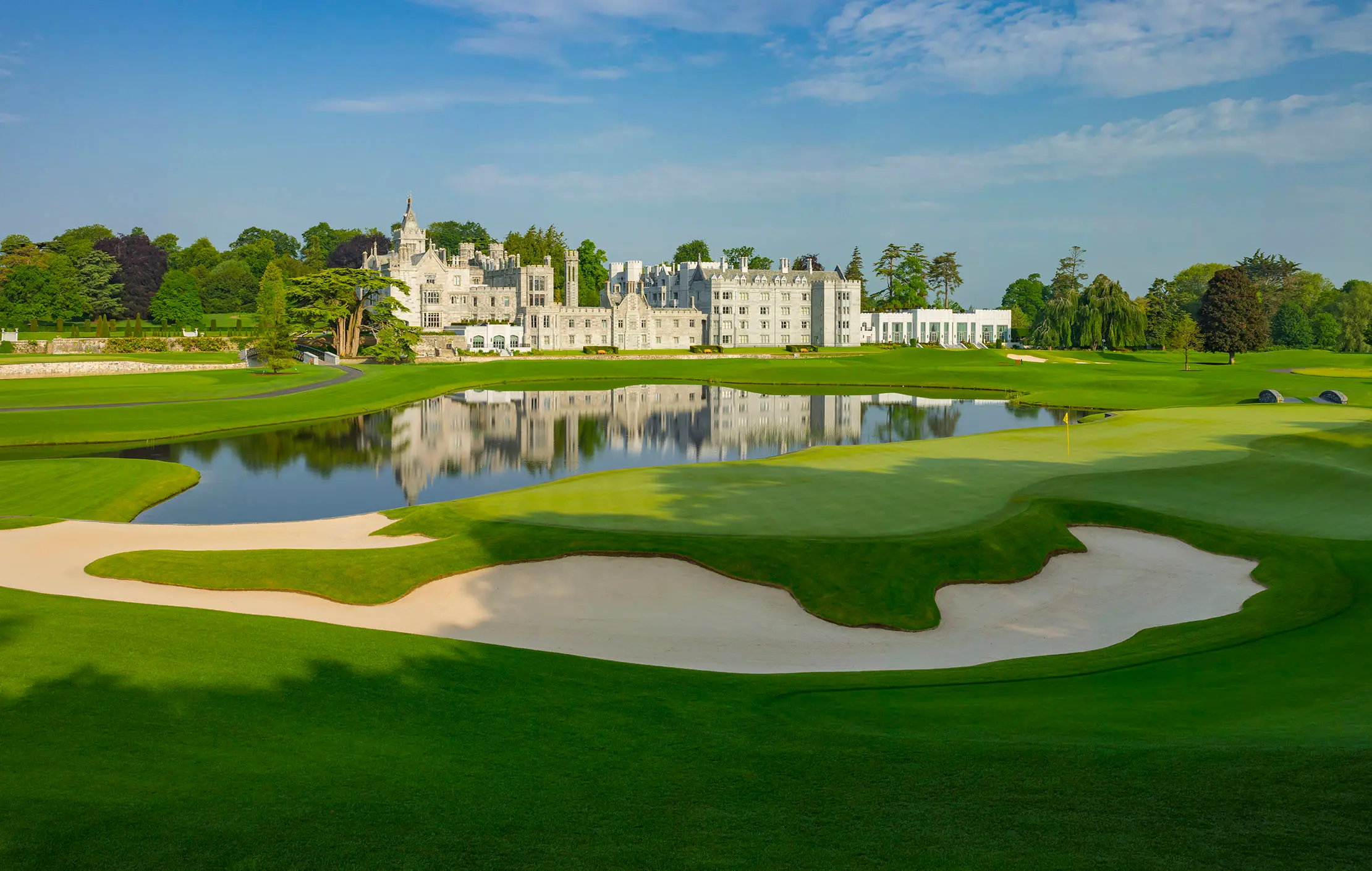 A sand bunker in the foreground with the castle and its reflection in the lake behind it.