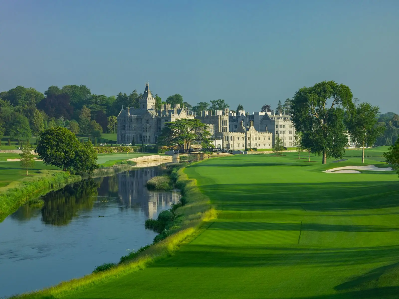 A view of the golf course with a wide river flowing beside the castle and manicured greens.