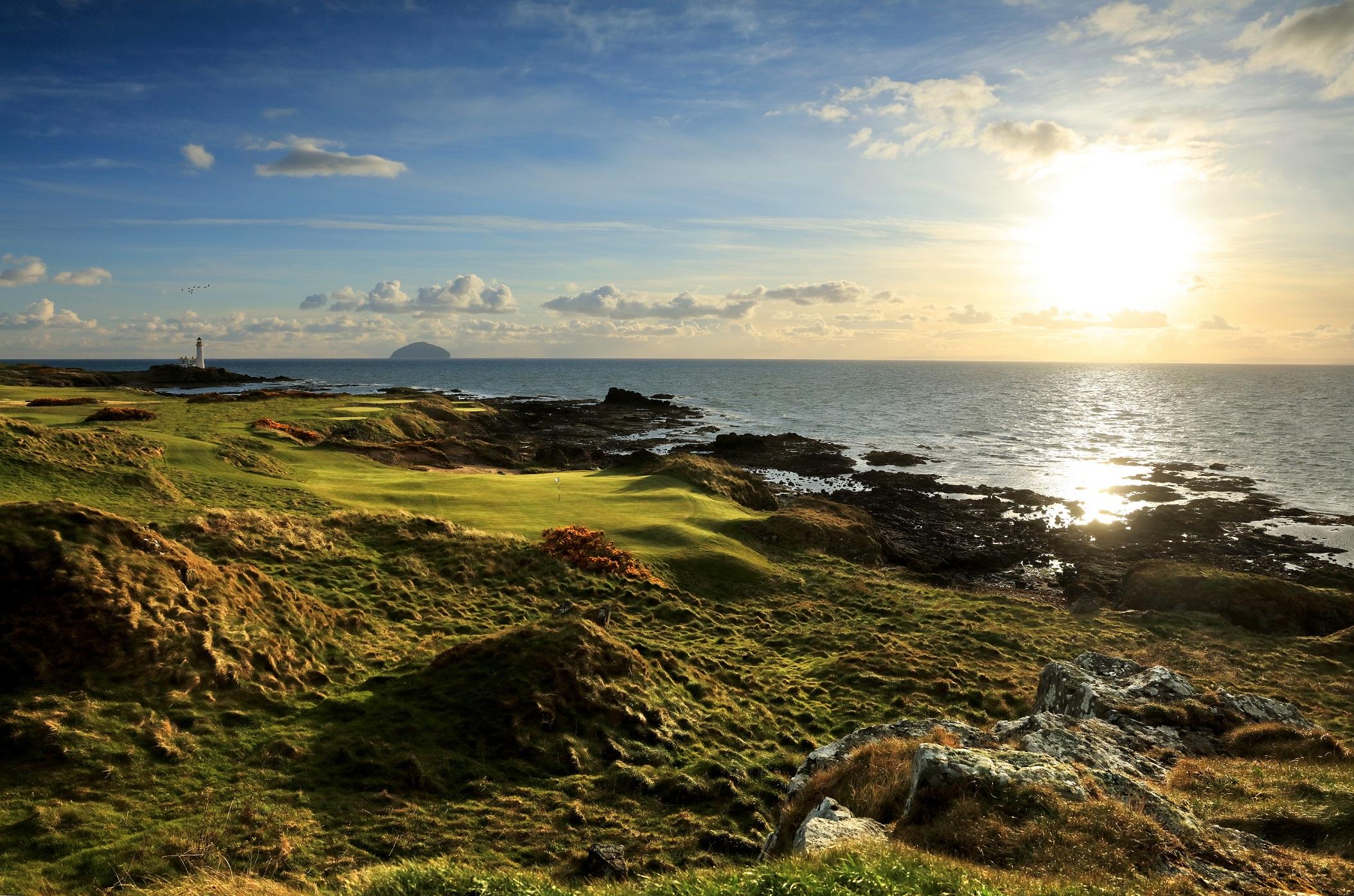 The sun setting over the rocky coastline, illuminating the greens of the golf course.