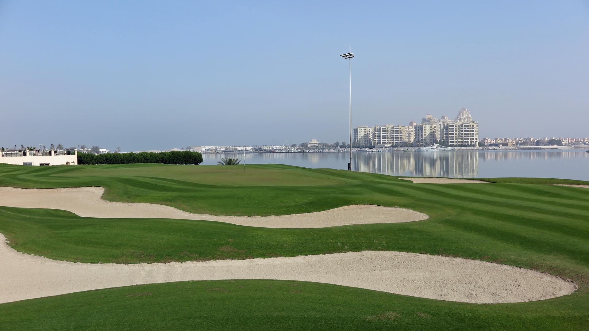 A smooth green surrounded by sand bunkers with coastal views