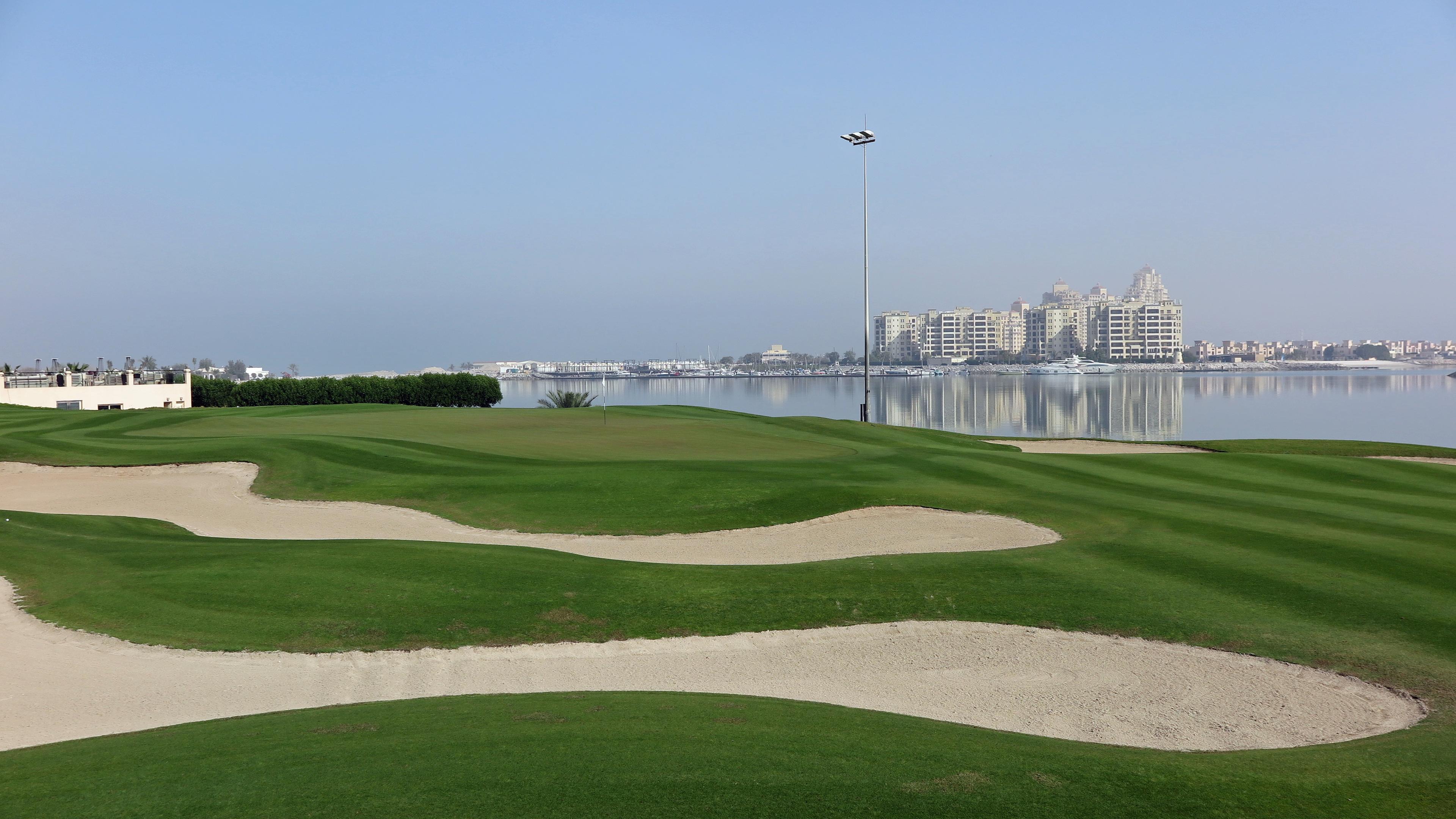 A smooth green surrounded by sand bunkers with coastal views