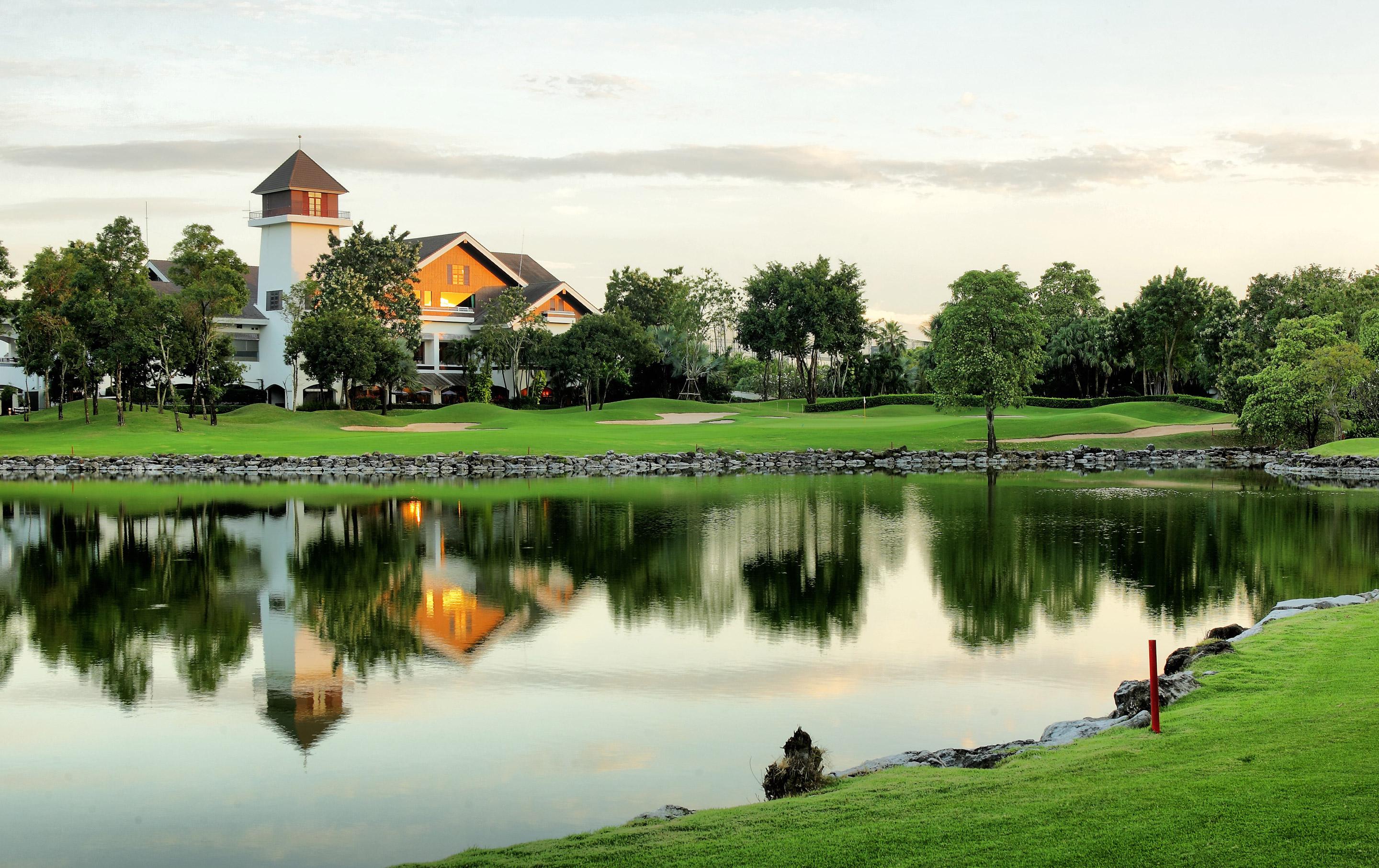 A picturesque golf club building reflected in a calm lake.