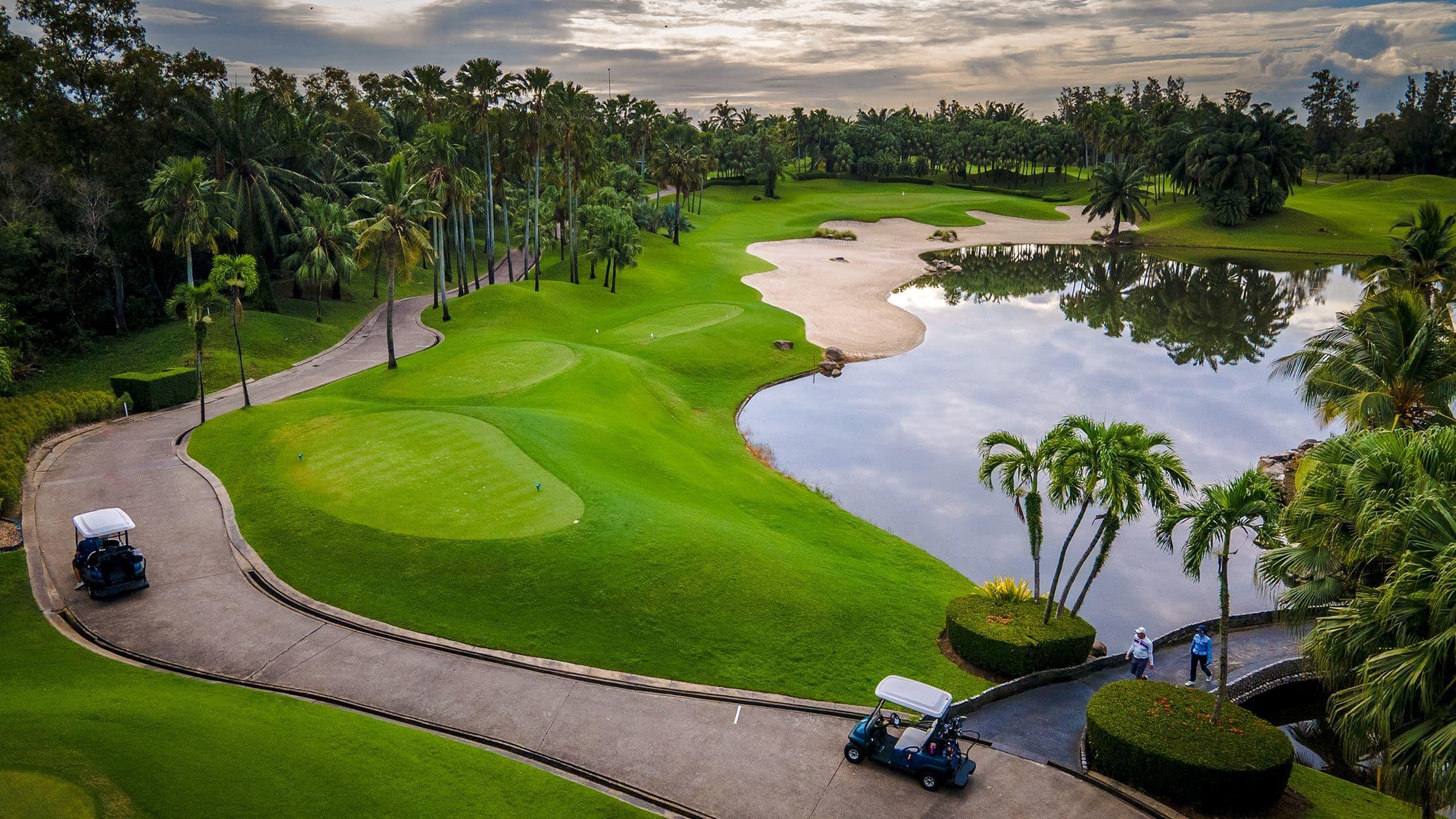 Golf carts on a scenic path beside a lake with palm trees.
