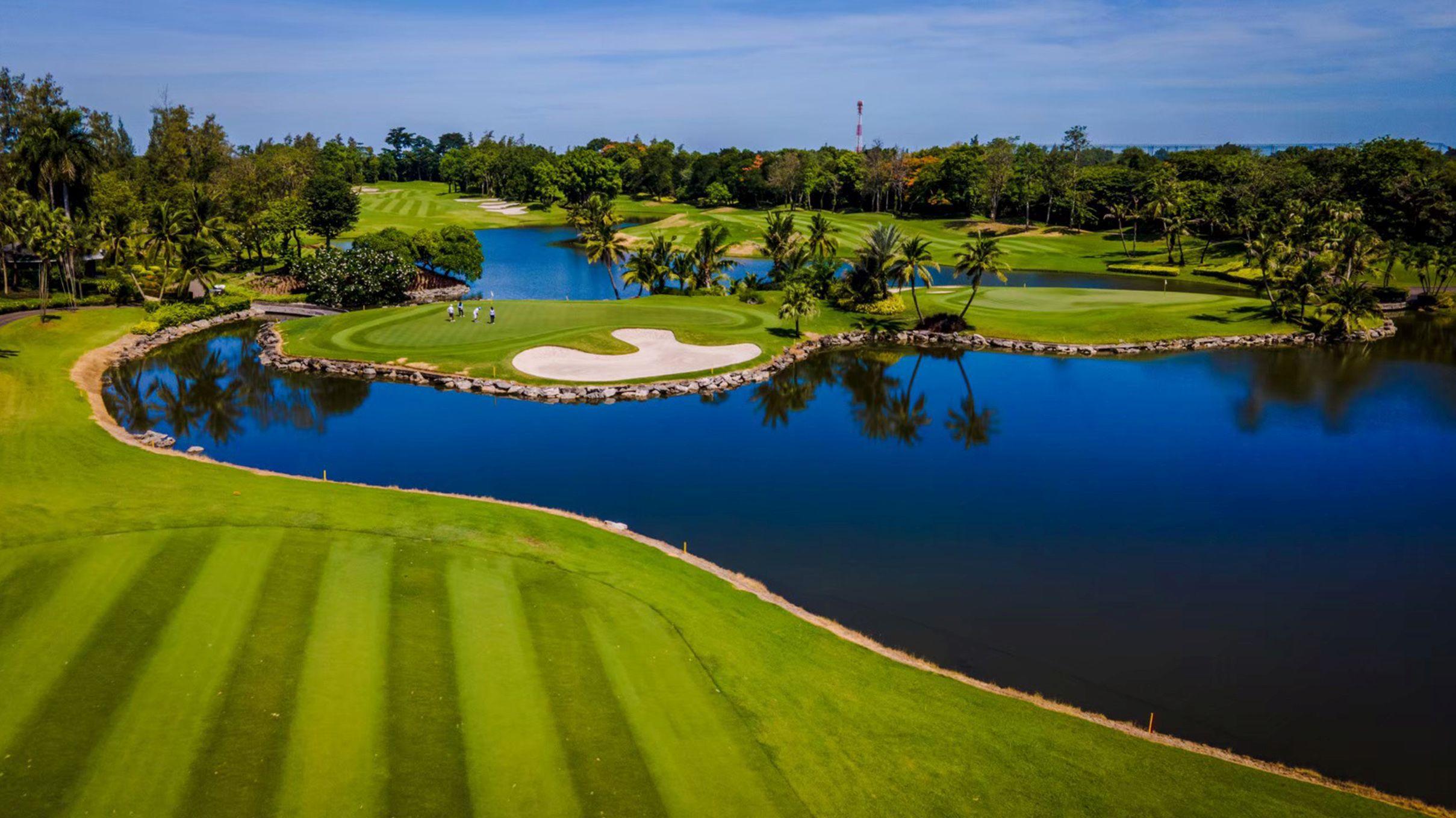 A vibrant golf course with sand bunkers and palm trees by a clear lake.