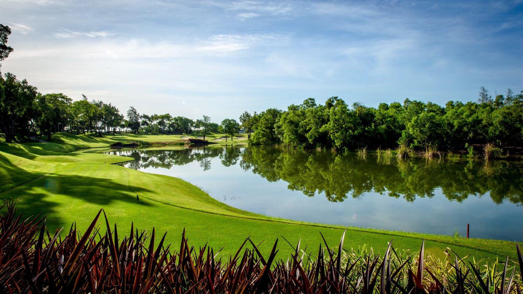 A serene golf course surrounded by a reflective lake and lush trees.