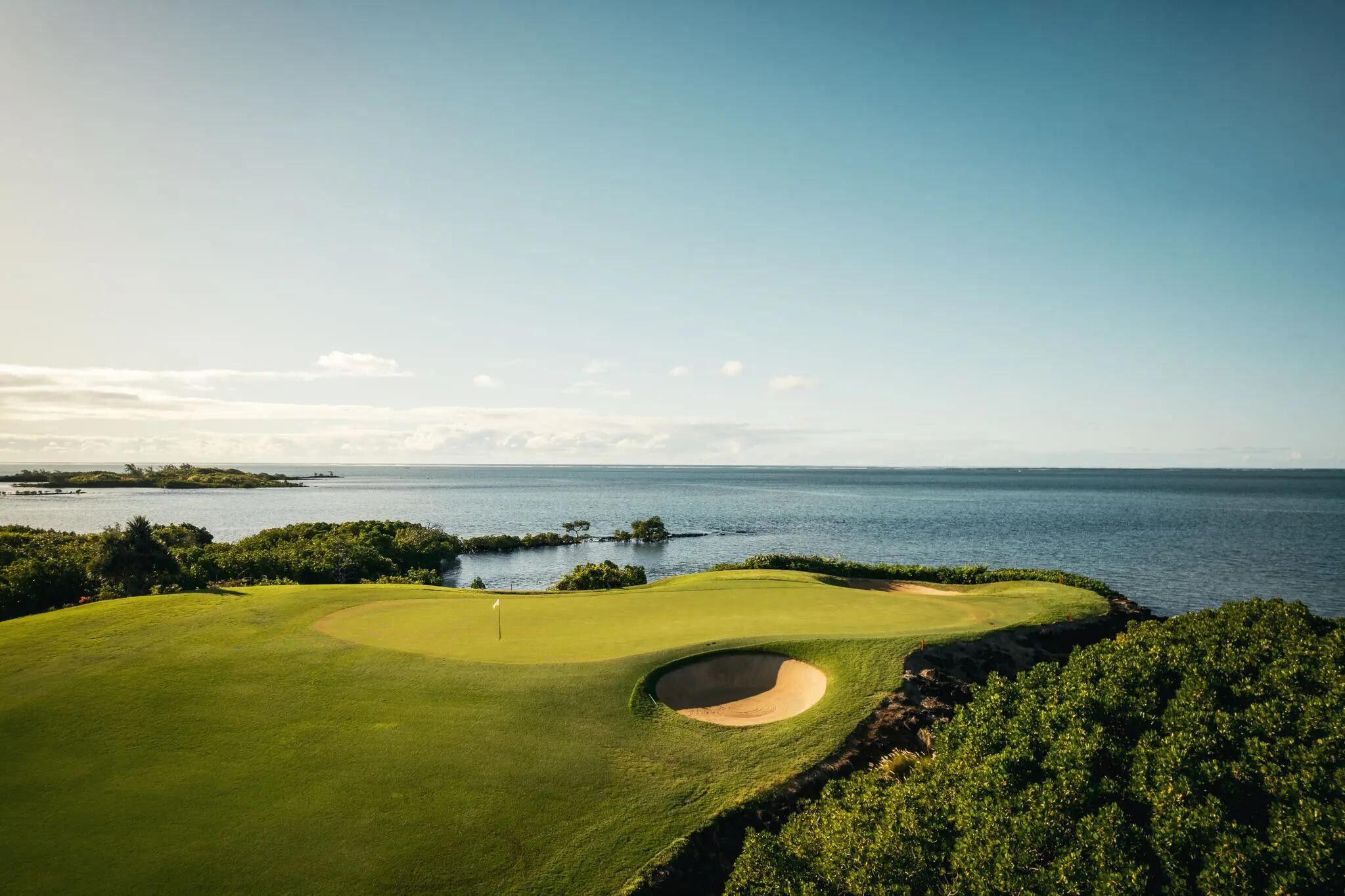 A smooth green surrounded by sand bunkers with coastal views