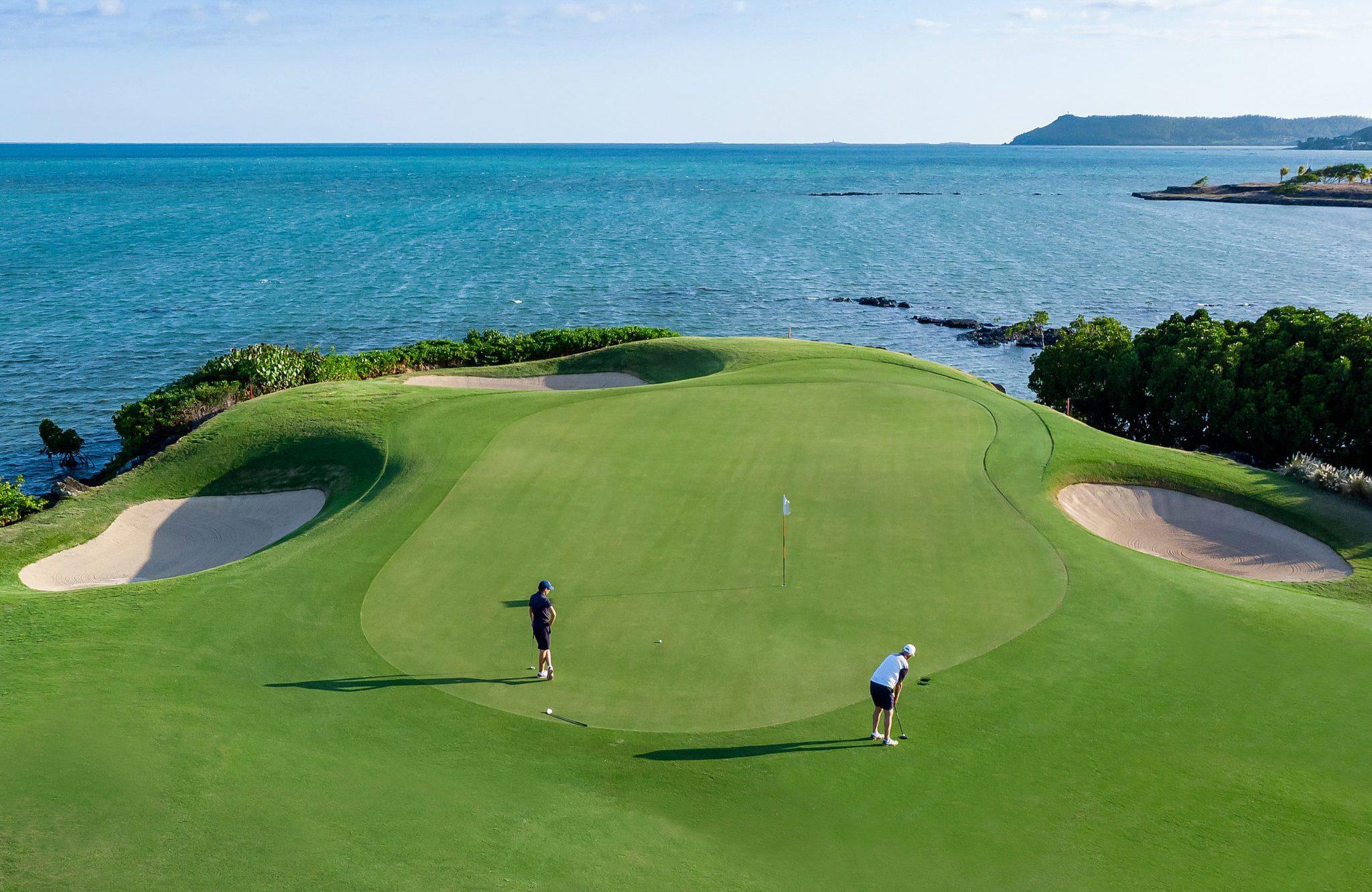 Golfers putting on a smooth green surrounded by sand bunkers with sea views