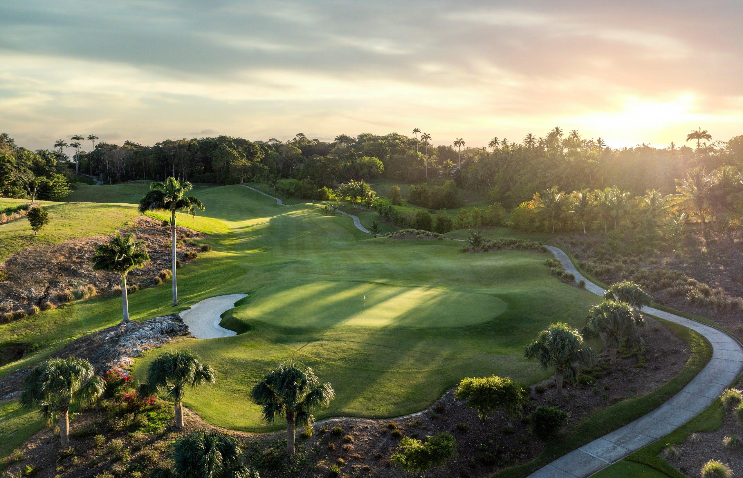 Sun setting over a straight fairway leading to a smooth green surrounded by palm trees