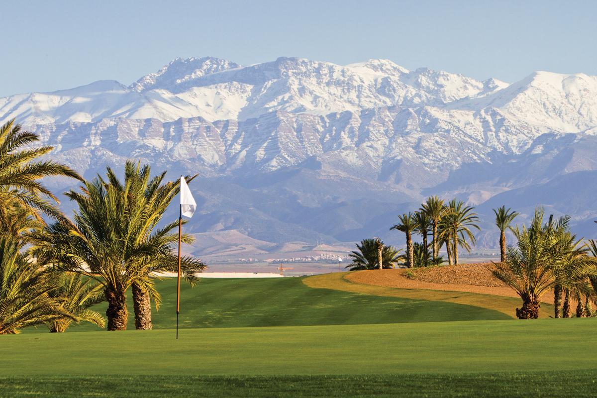 Ice topped mountains towering over a smooth green with a white flagstick