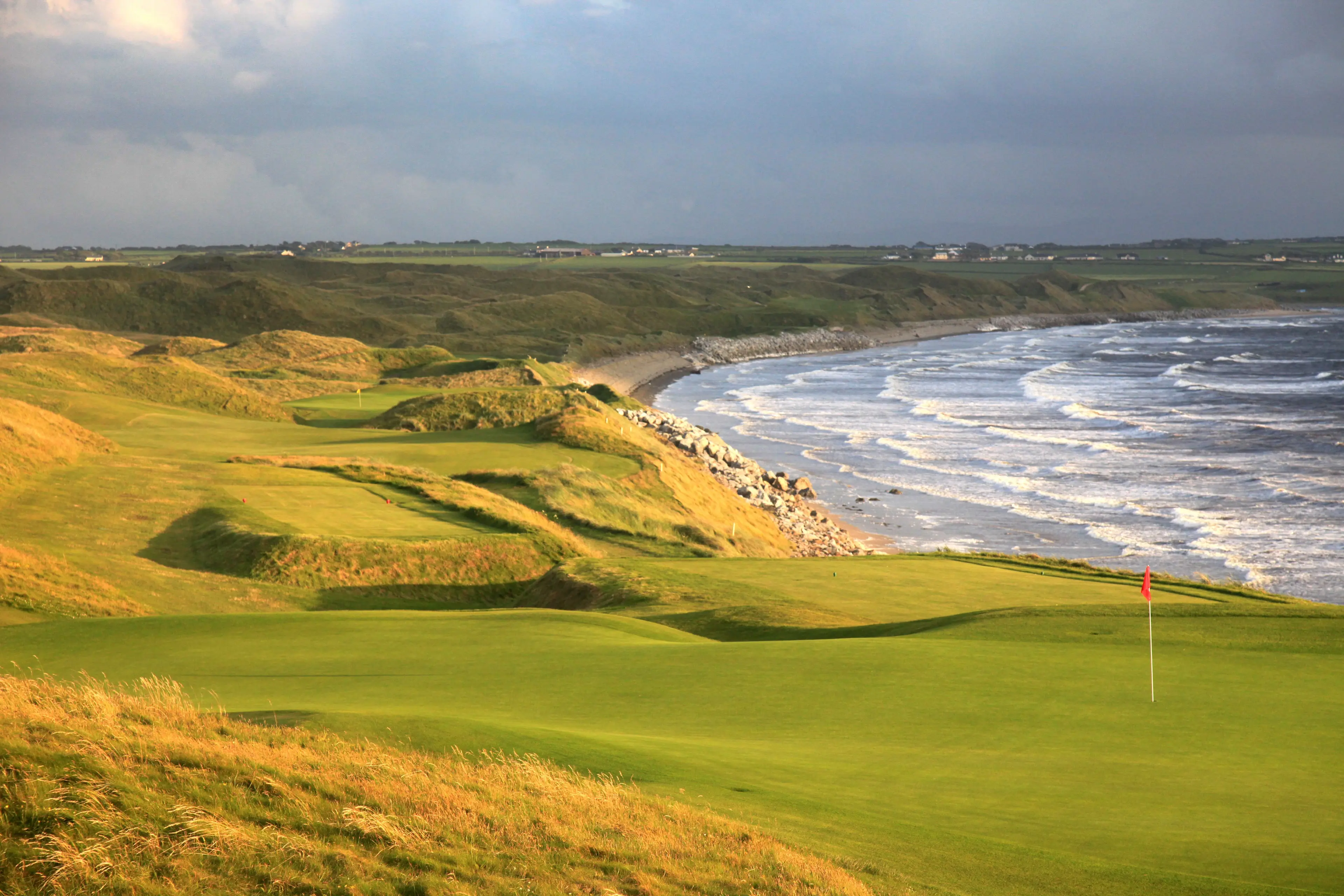 A fairway runs along the rugged coast with waves breaking against the rocky shore.