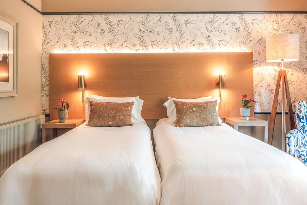 Twin bed room at The Belfry hotel illuminated by lamps following a simple wood design
