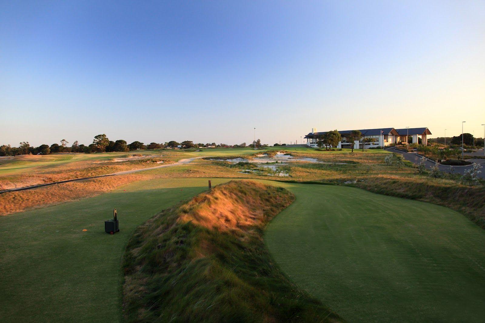 A wide, open golf course at sunset with sandy terrain and a clubhouse in the distance.