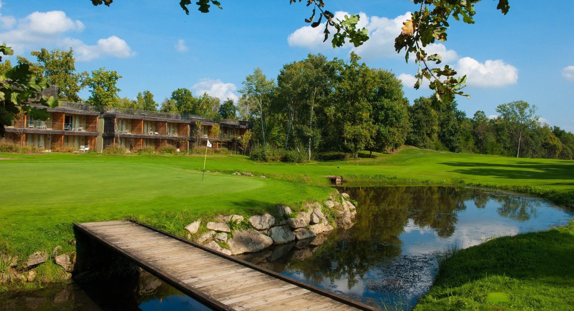 A charming wooden lodge next to a reflective pond and golf green.