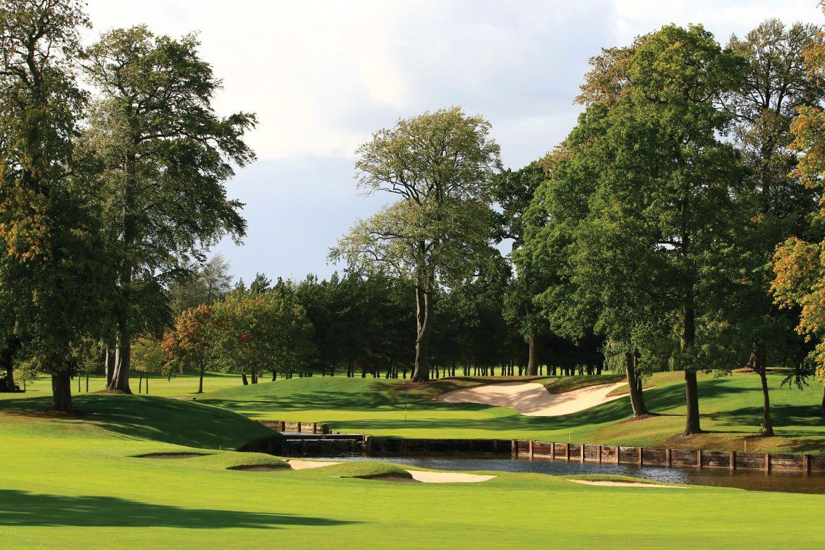Green protected by water and a large bunker, surrounded by trees.