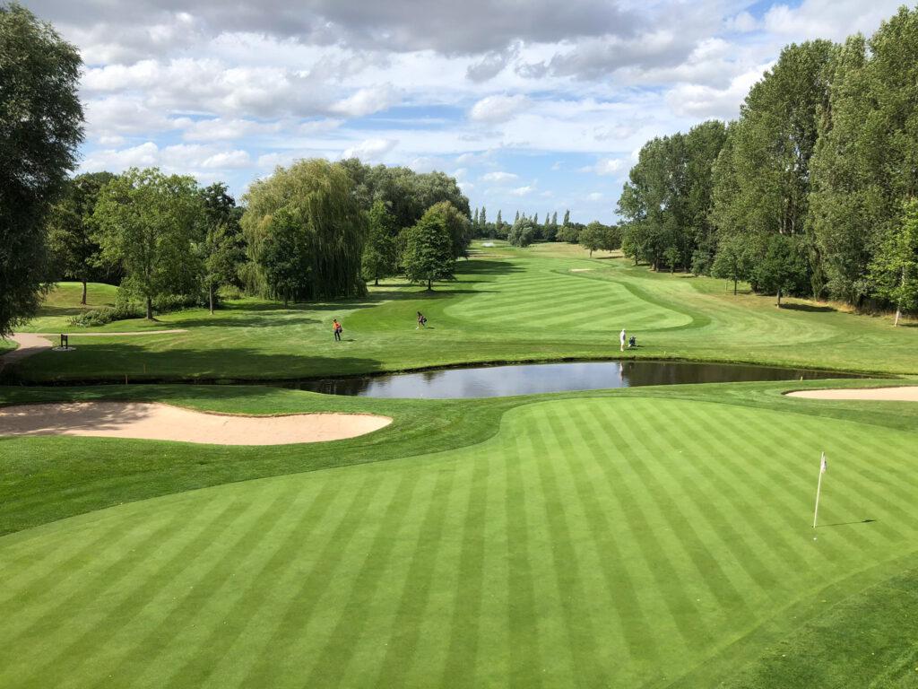 Pond and bunkers near the green with golfers in the distance.