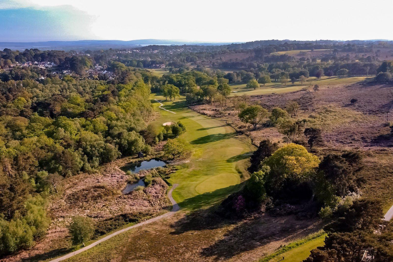 An aerial view of a scenic golf course surrounded by dense woodland and ponds.
