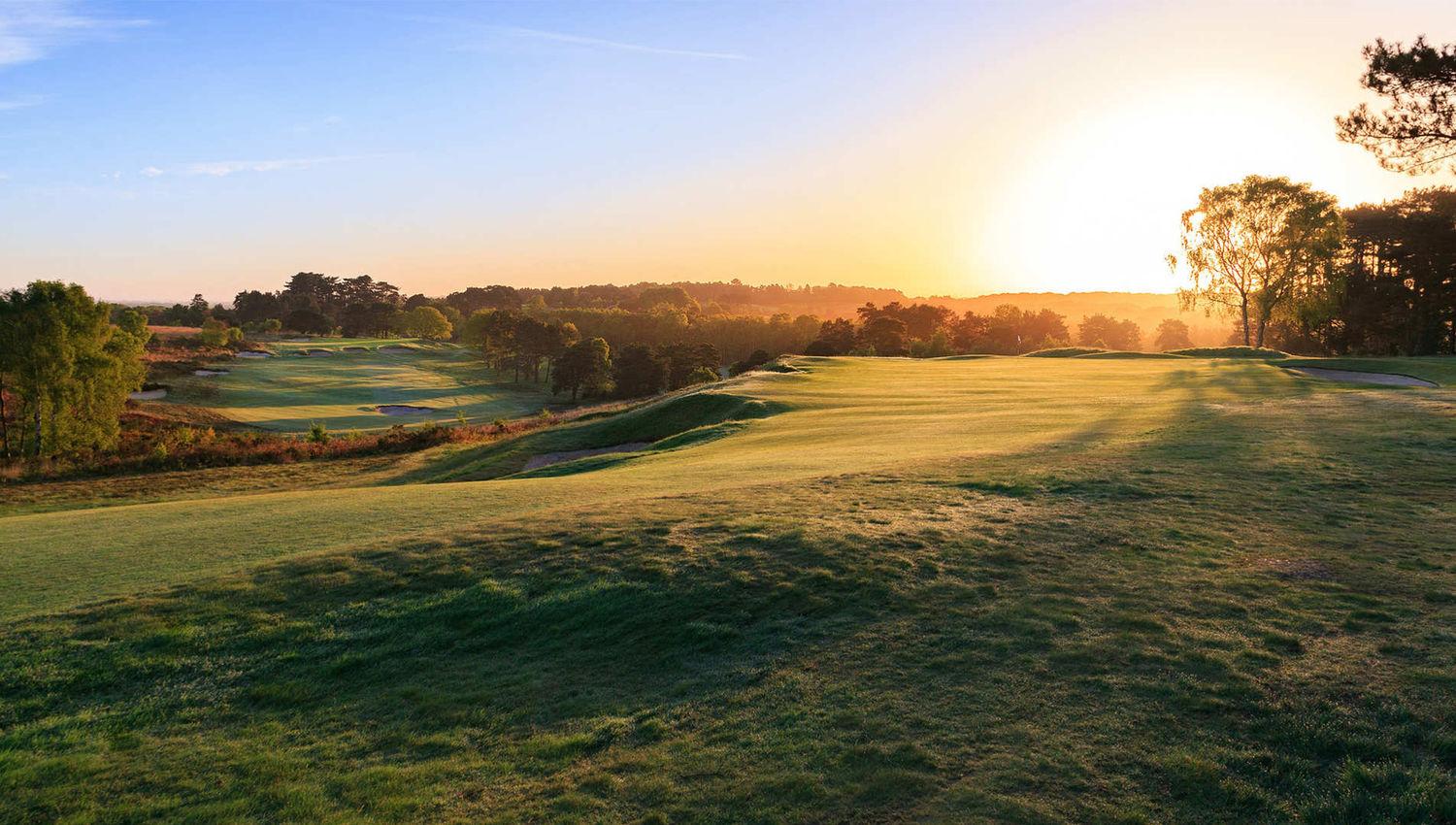 A golden sunrise casting long shadows across the rolling fairways of a golf course.