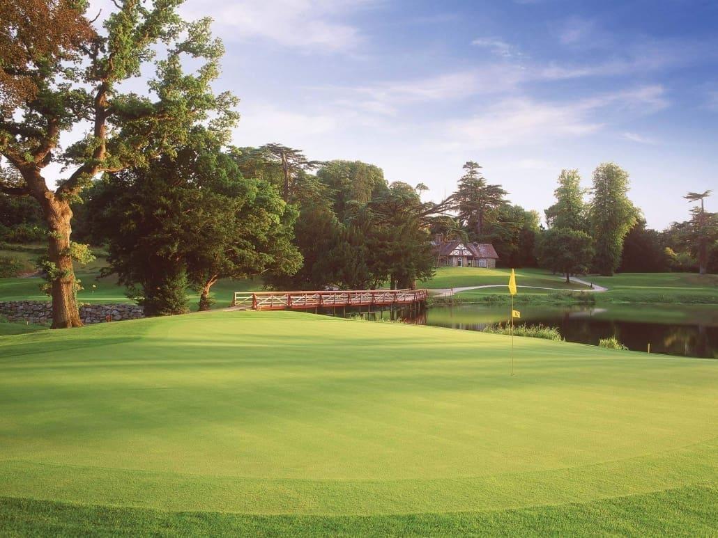 A pristine green with a yellow flagstick overlooks a serene water hazard.