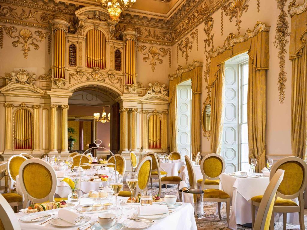 A grand dining room with ornate gold decor and round tables set for fine dining.