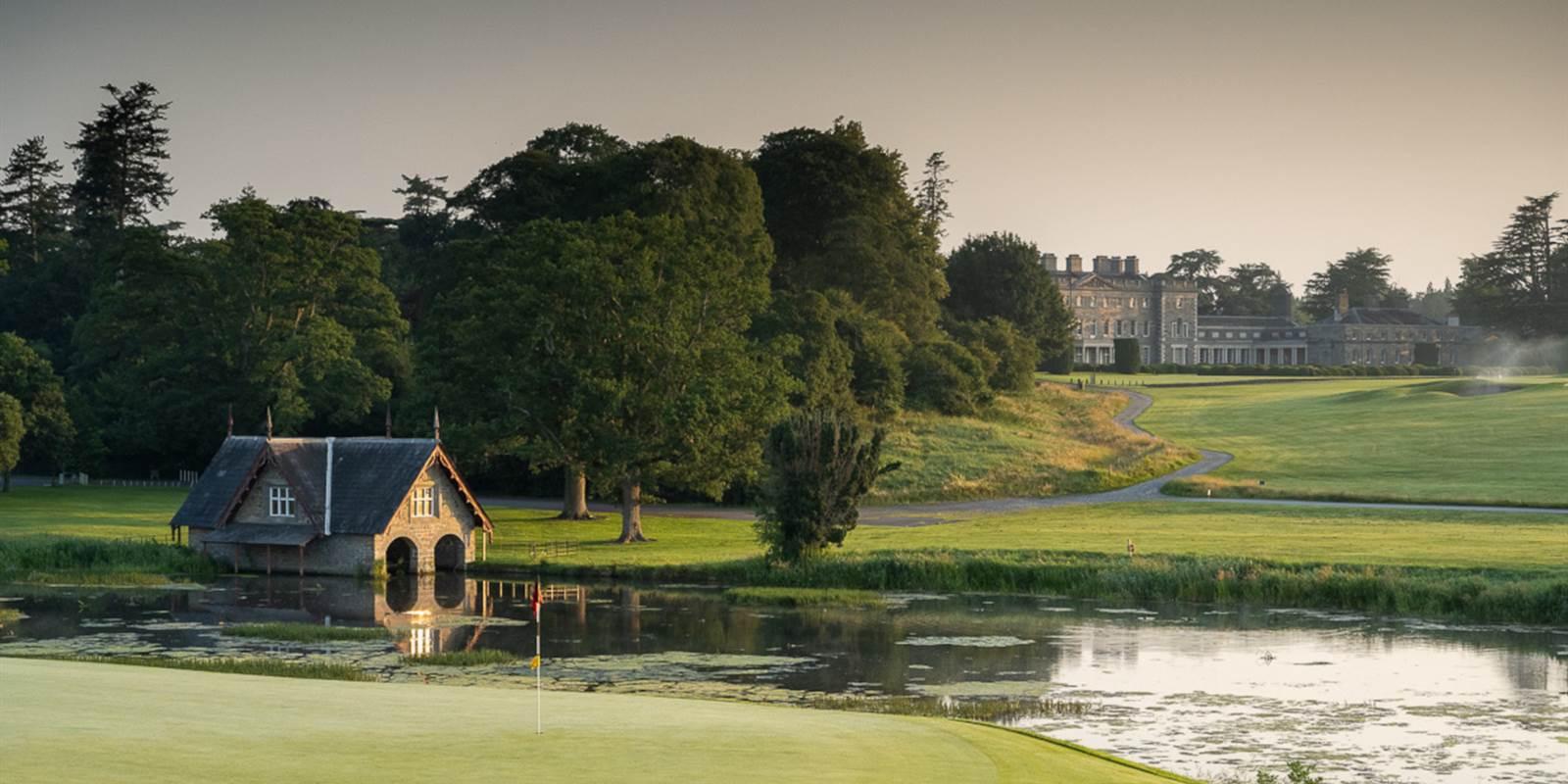 The green sits beside a calm pond with reflections of the boathouse.
