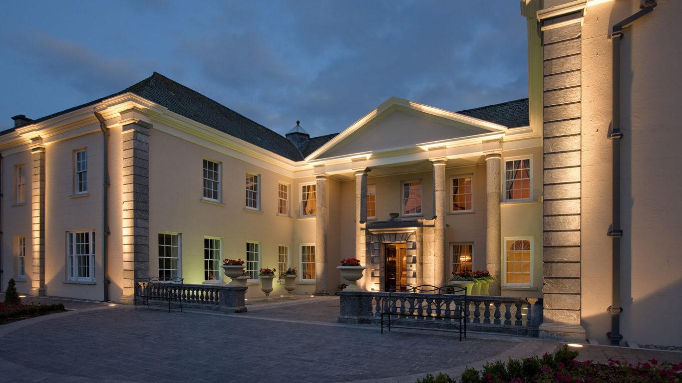The grand entrance to Castlemartyr Resort, beautifully lit at dusk with classical architecture.