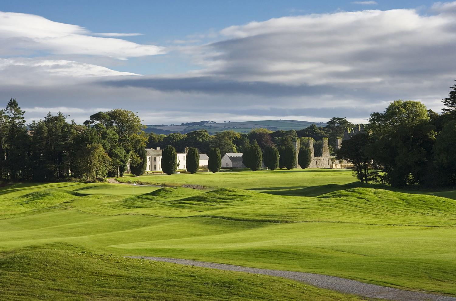 Rolling fairways leading to historic castle ruins set against a dramatic sky.