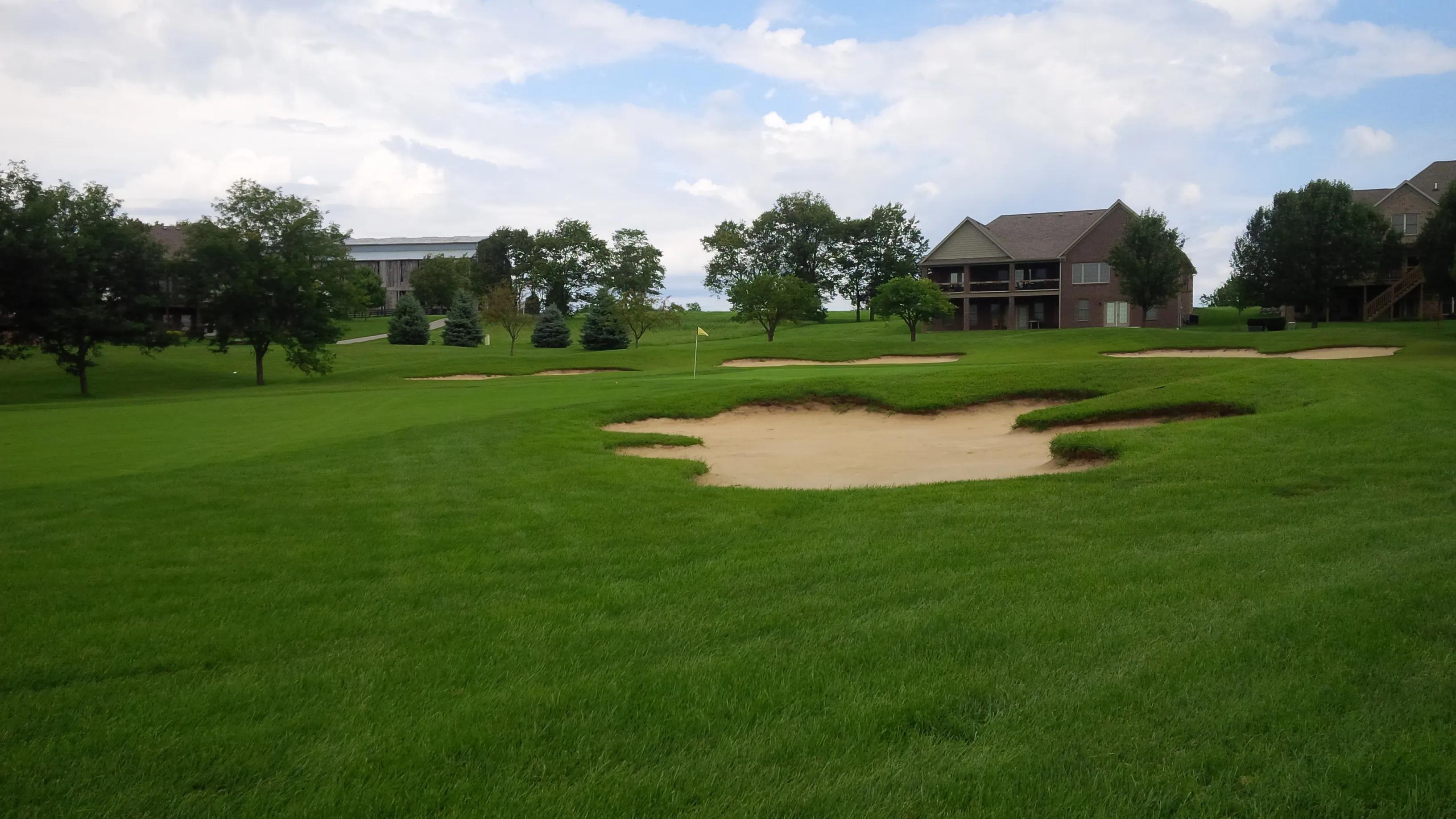 Sand bunkers frame a putting green on a beautifully maintained golf course near residential homes.