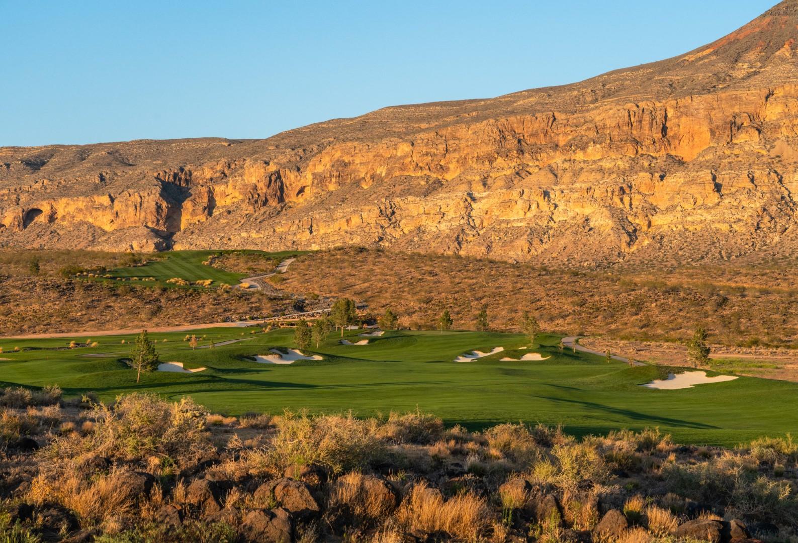 Green fairways contrast against rugged desert cliffs at sunset.