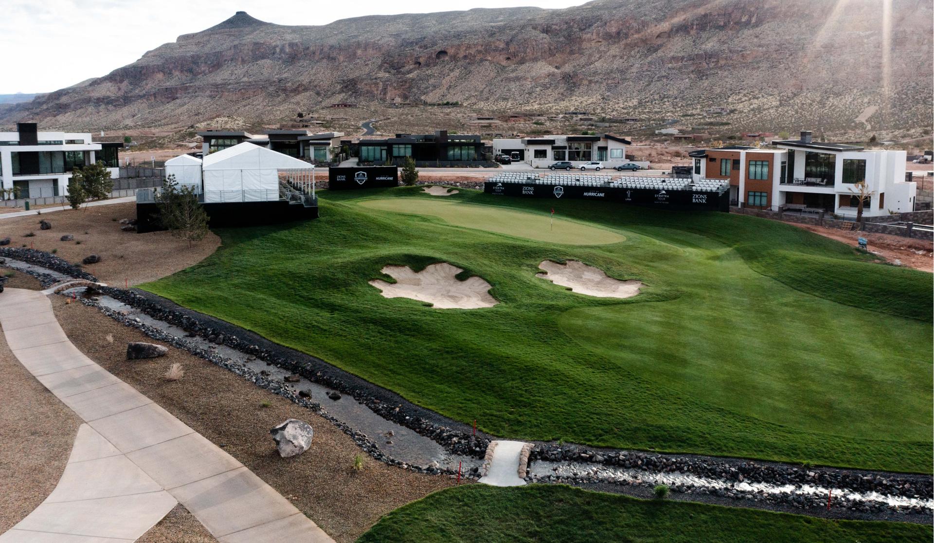 A modern golf green with bunkers sits in a residential desert setting.