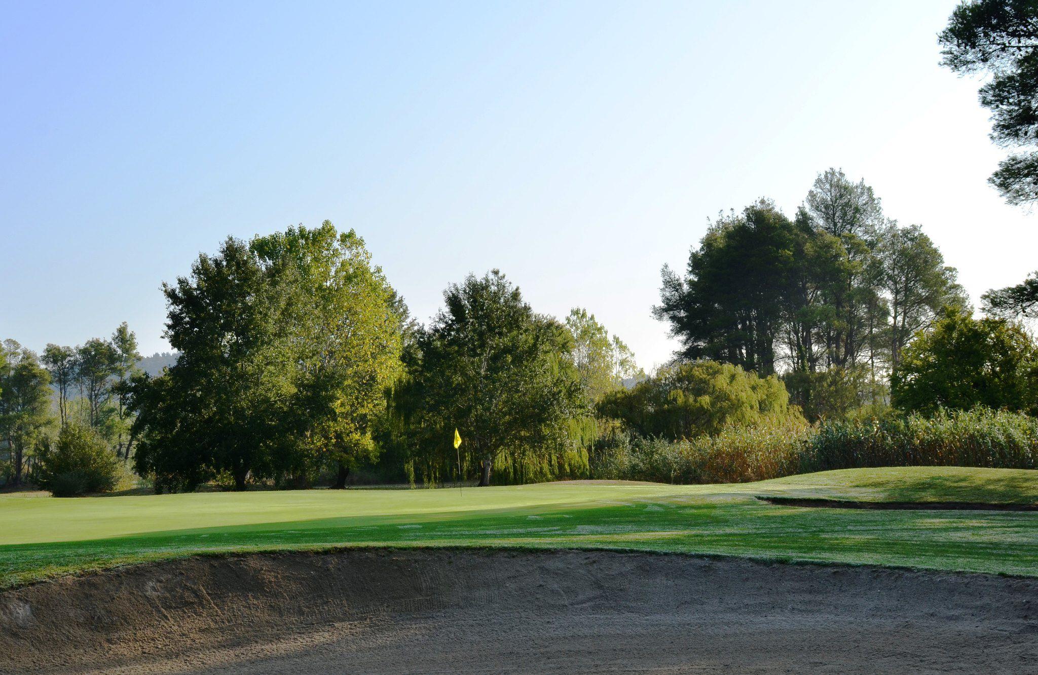 Two large sand bunkers surrounding a manicured green under clear blue skies