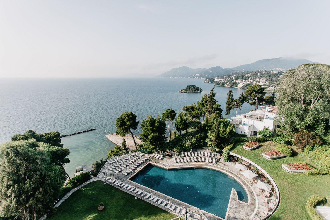 Swimming pool at Corfu Holiday Palace surrounded by sunbeds with coastal views