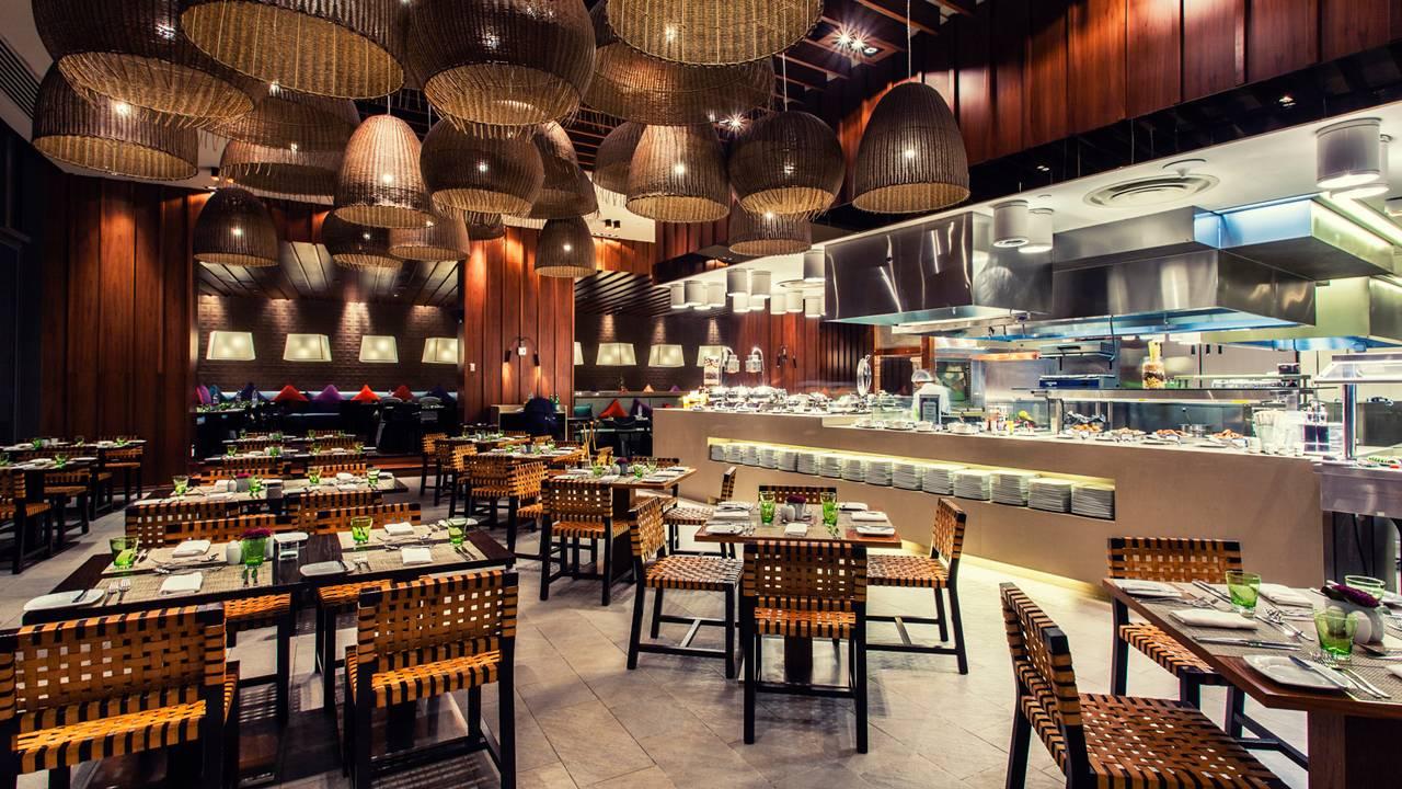 A luxurious restaurant at the hotel with a open kitchen feature alongside straw dining chairs