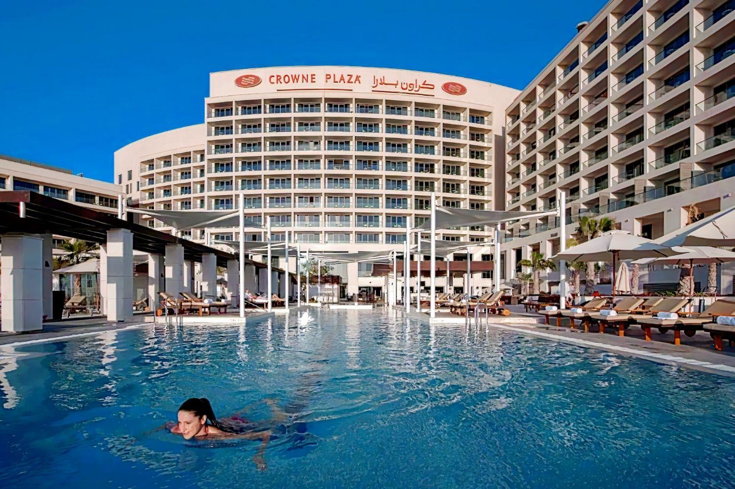 An outdoor swimming pool at the hotel surrounded by sunbeds with the hotel building towering over