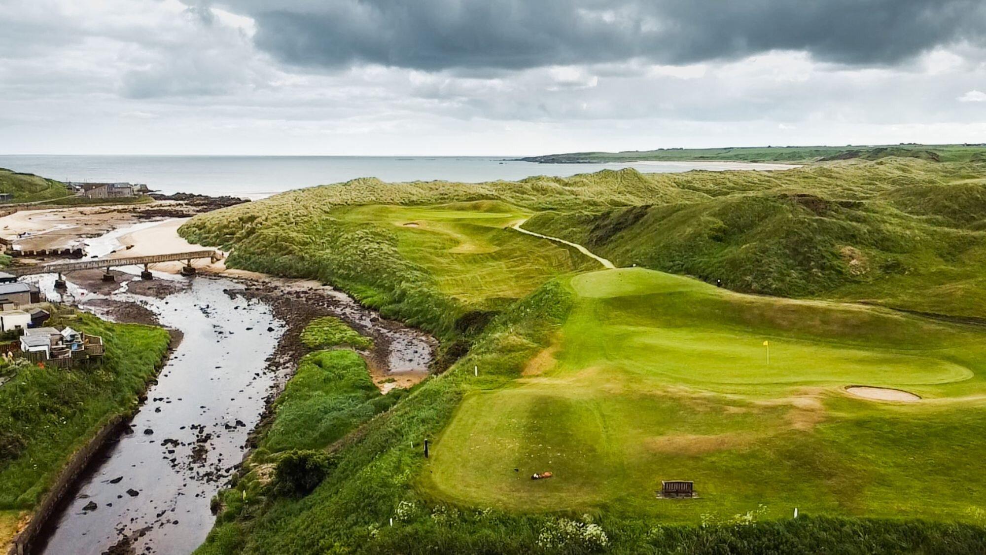Overhead shot of the wide fairways and manicured green with water hazard running besides the course