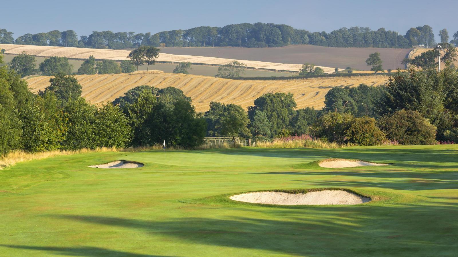 Rolling fairways framed by golden fields and lush green trees.