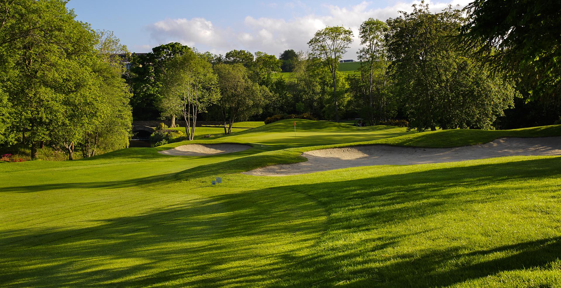 A lush golf course with sand bunkers and a green surrounded by trees.
