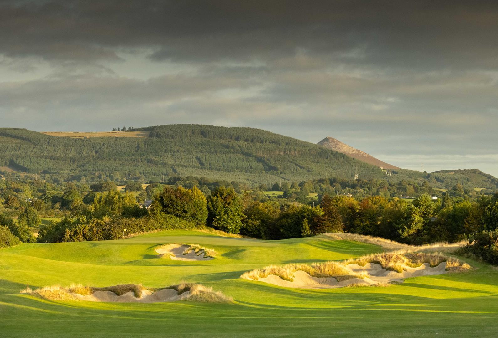 A wide, open fairway with rugged bunkers framed by scenic hills.