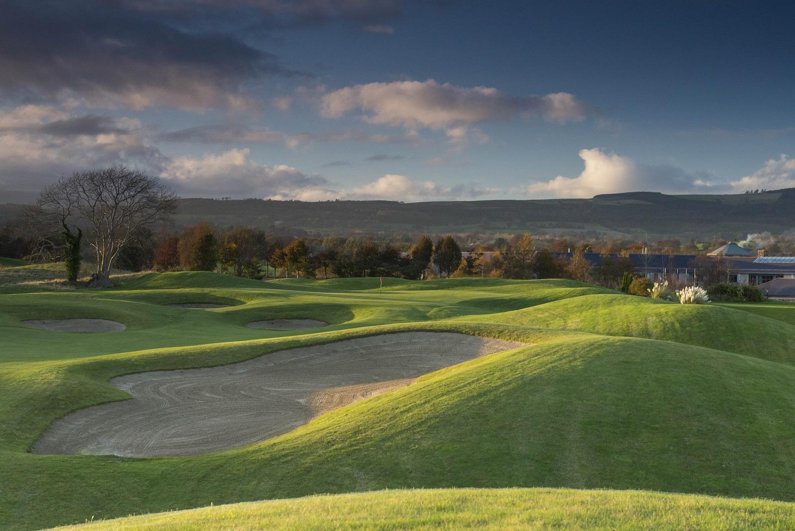 Sand bunkers and a green with dramatic clouds and hills in the distance.