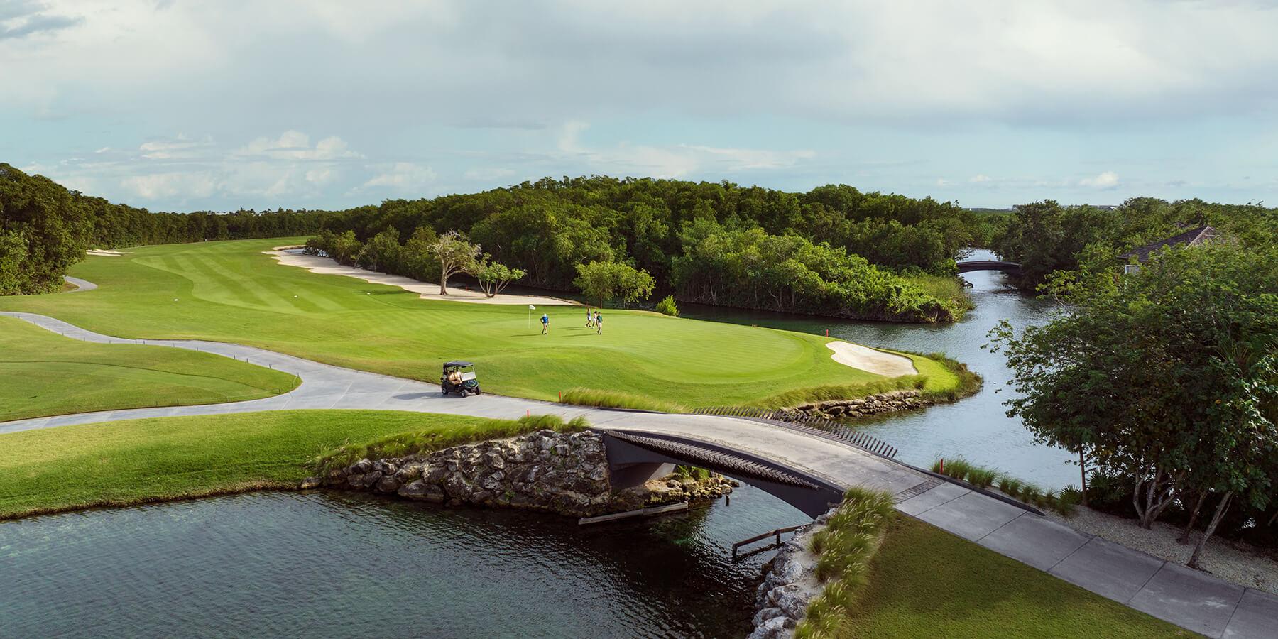 A stone bridge big enough for buggies to navigate the water hazard next to a smooth green