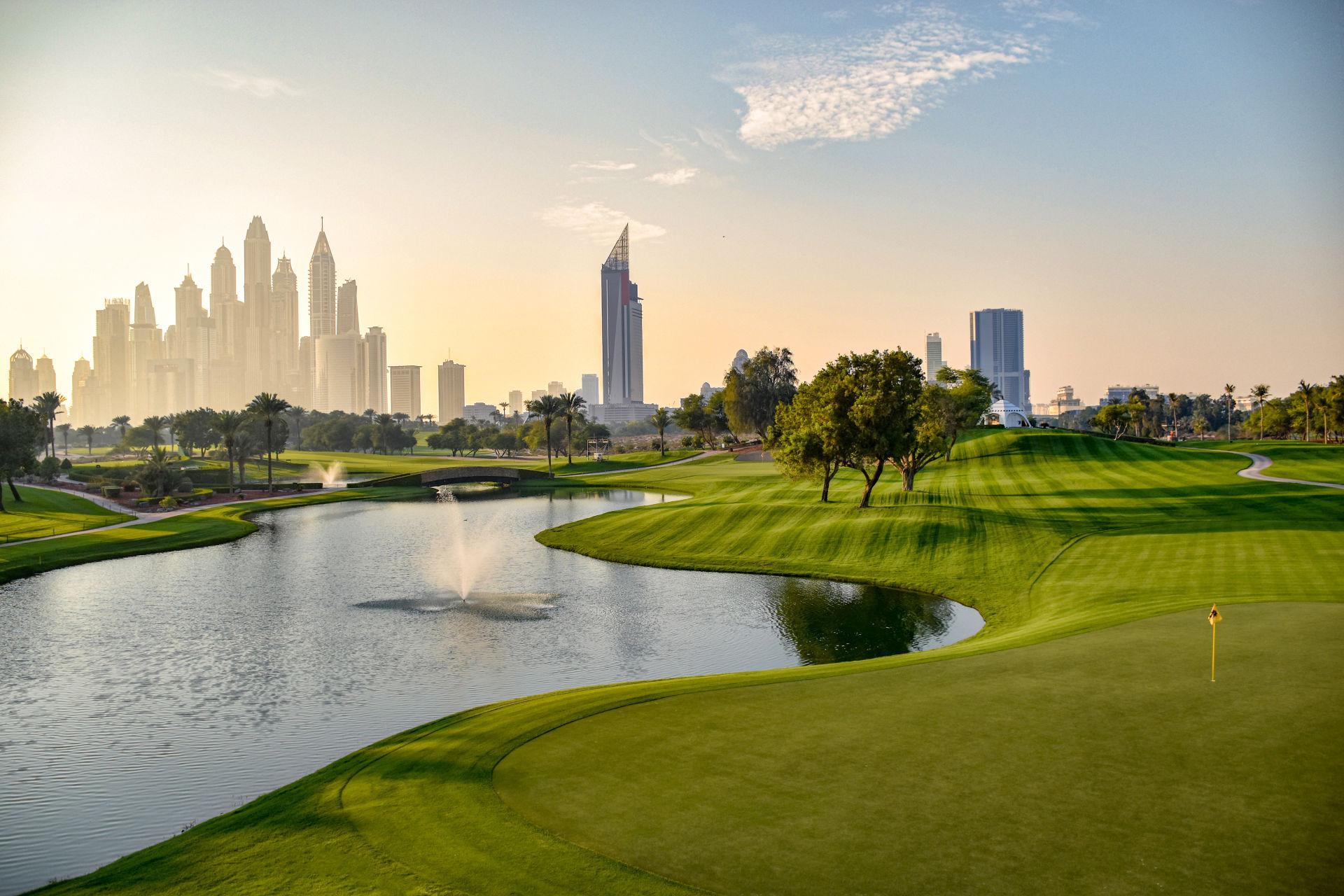 A stunning golf course with water features and a skyline backdrop at sunrise.