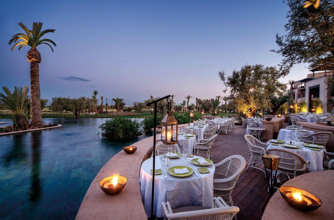 An outdoor poolside dining area being lit up by candles and lamps in the evening