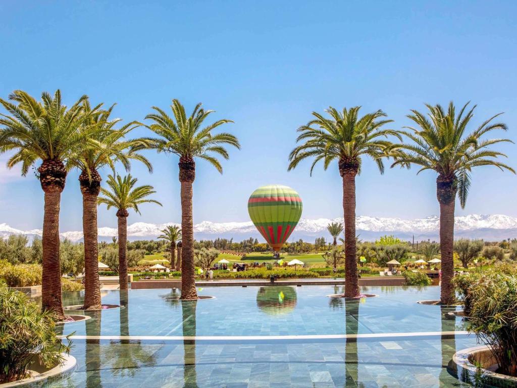 A swimming pool framed by palm trees with a hot air balloon in the distance