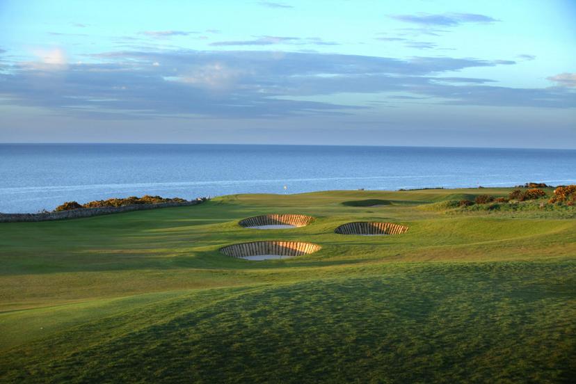A stunning links golf course with pot bunkers overlooking the calm blue sea.