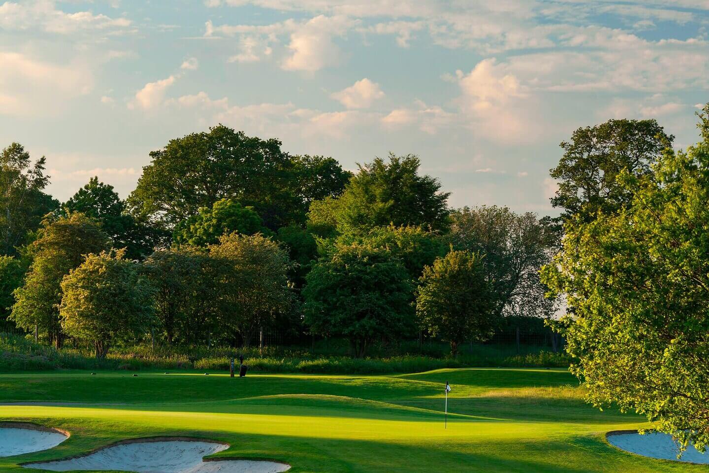 Sand bunkers around a green surrounded by lush trees.