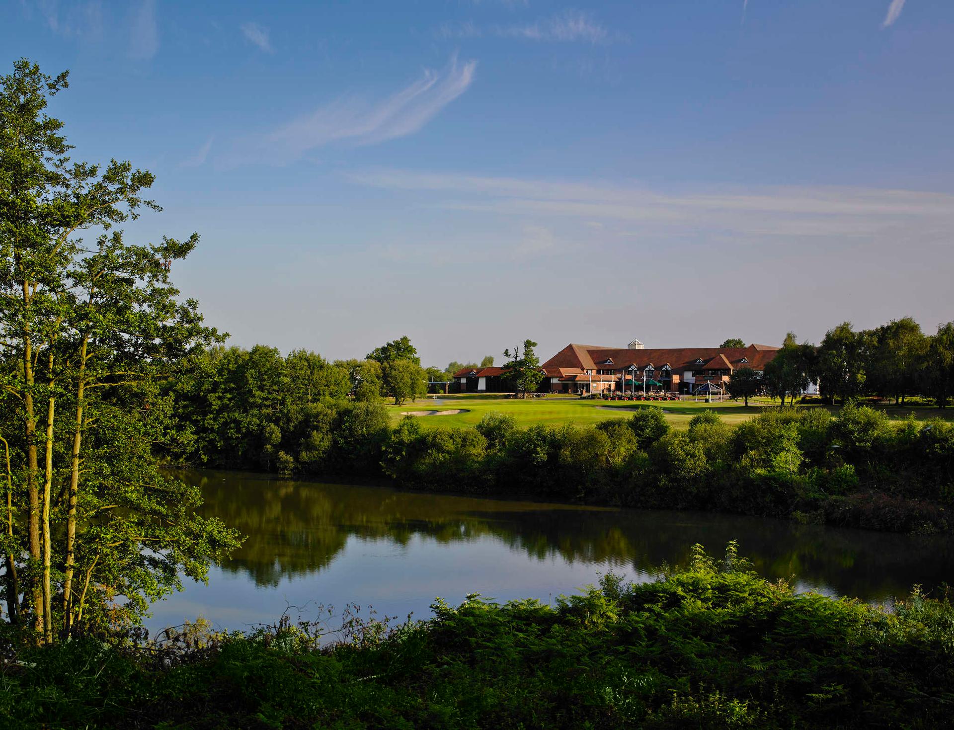 The Forest of Arden clubhouse overlooking the green leading to a pond under blue skies