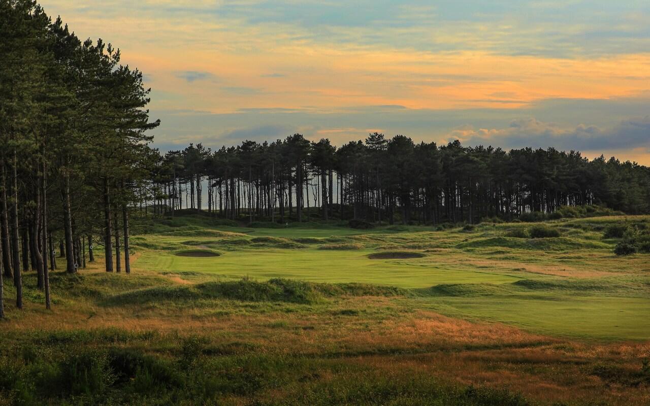 A sunset view of the golf course with lush greens framed by a dense forest.